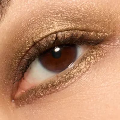 Close-up of a brown eye with shimmery bronze-gold liner smudged along upper and lower lash lines.