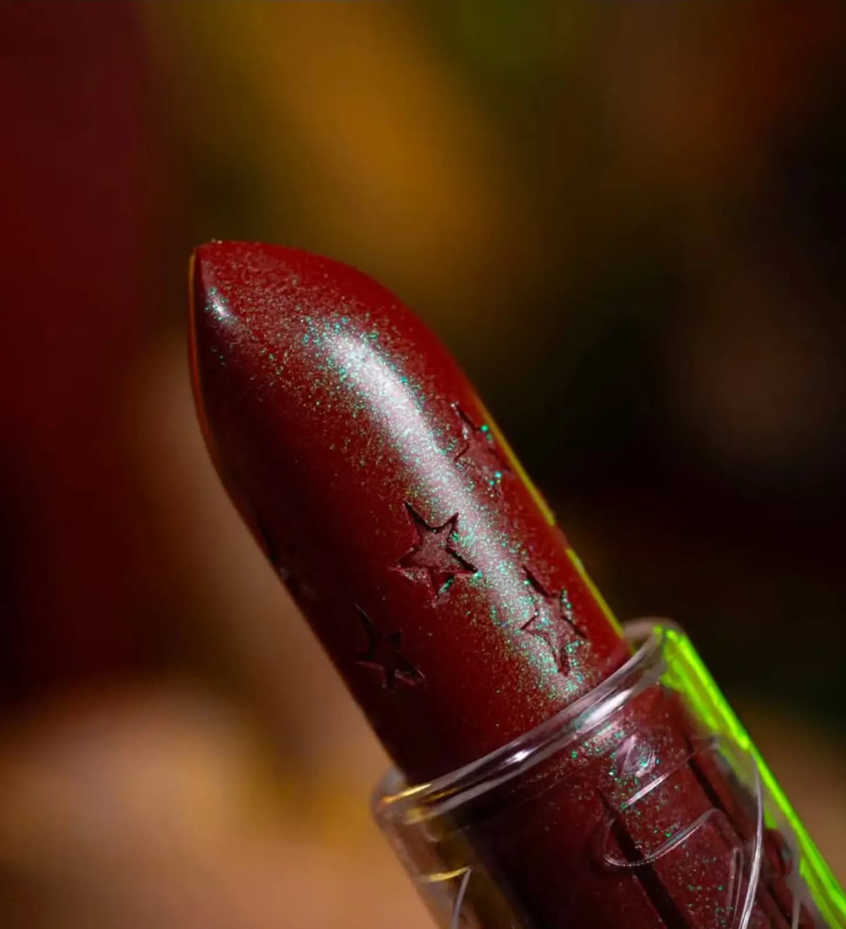 Close-up of the burgundy balm bullet with embossed stars and fine green-blue sparkle glinting in the light