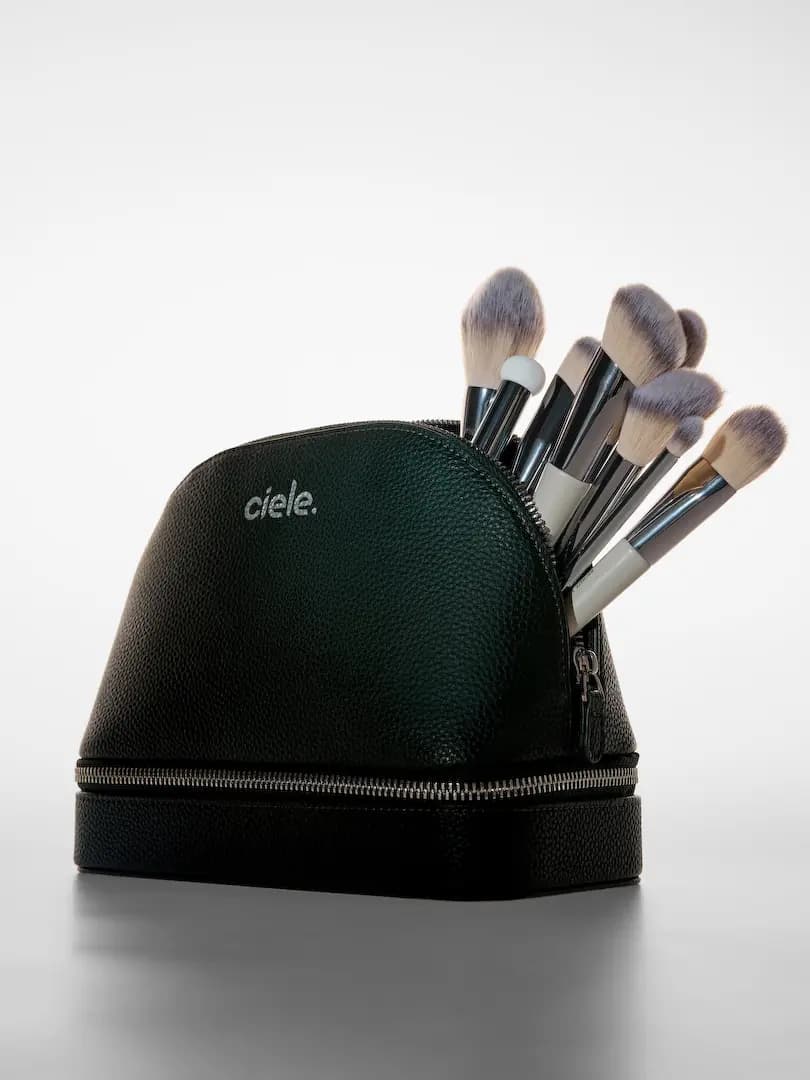 Dark green pebbled ciele makeup bag with silver zippers, a bundle of white-handled brushes poking out the top