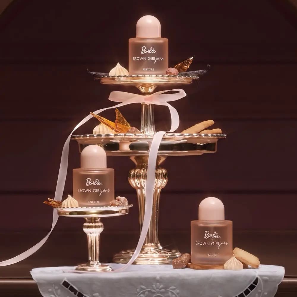 Three peach bottles on gilded cake stands with meringues, caramel shards and a pink satin ribbon against dark wood