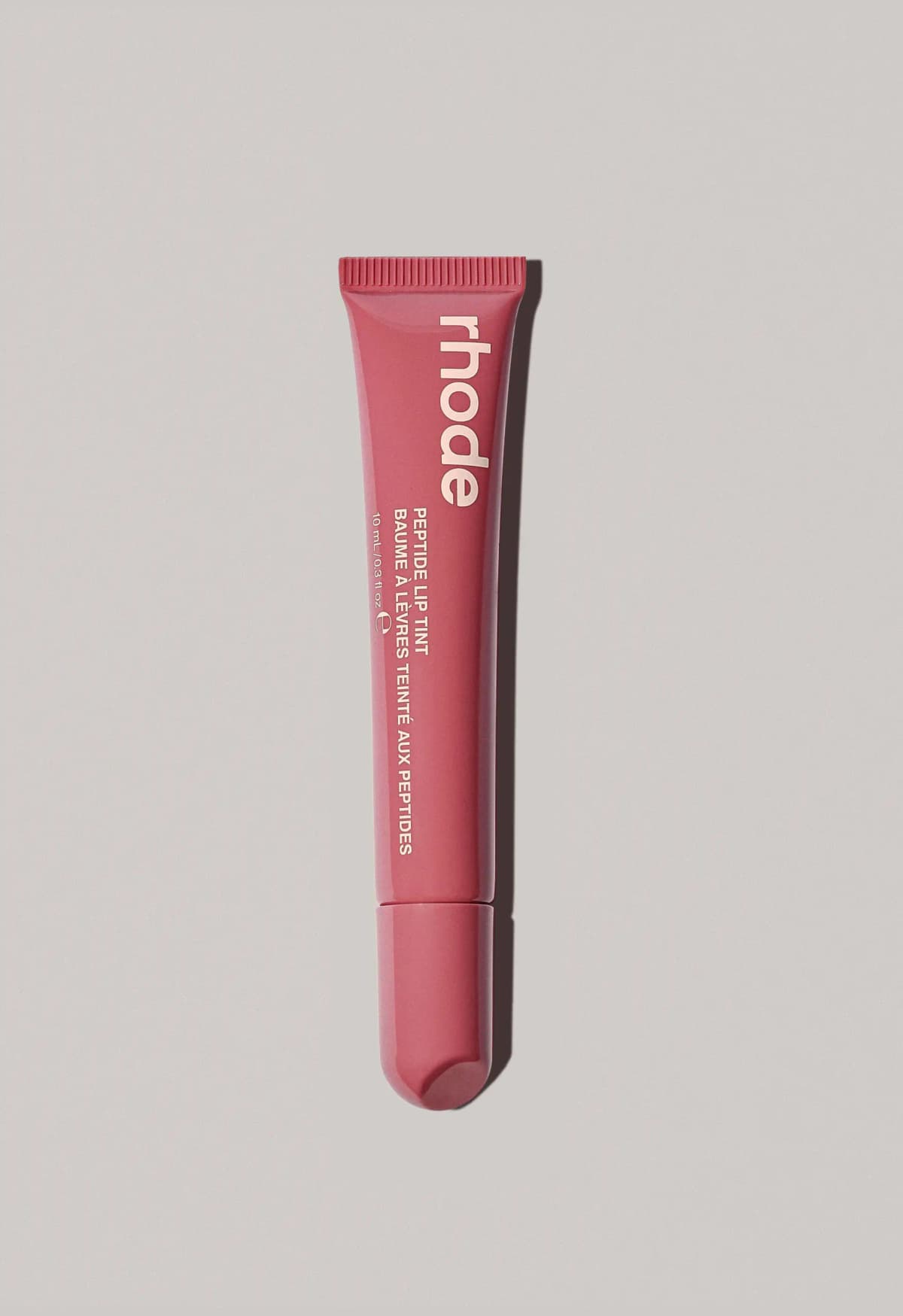 Rosy raspberry-red rhode lip tint tube with pale peach lettering on a grey surface