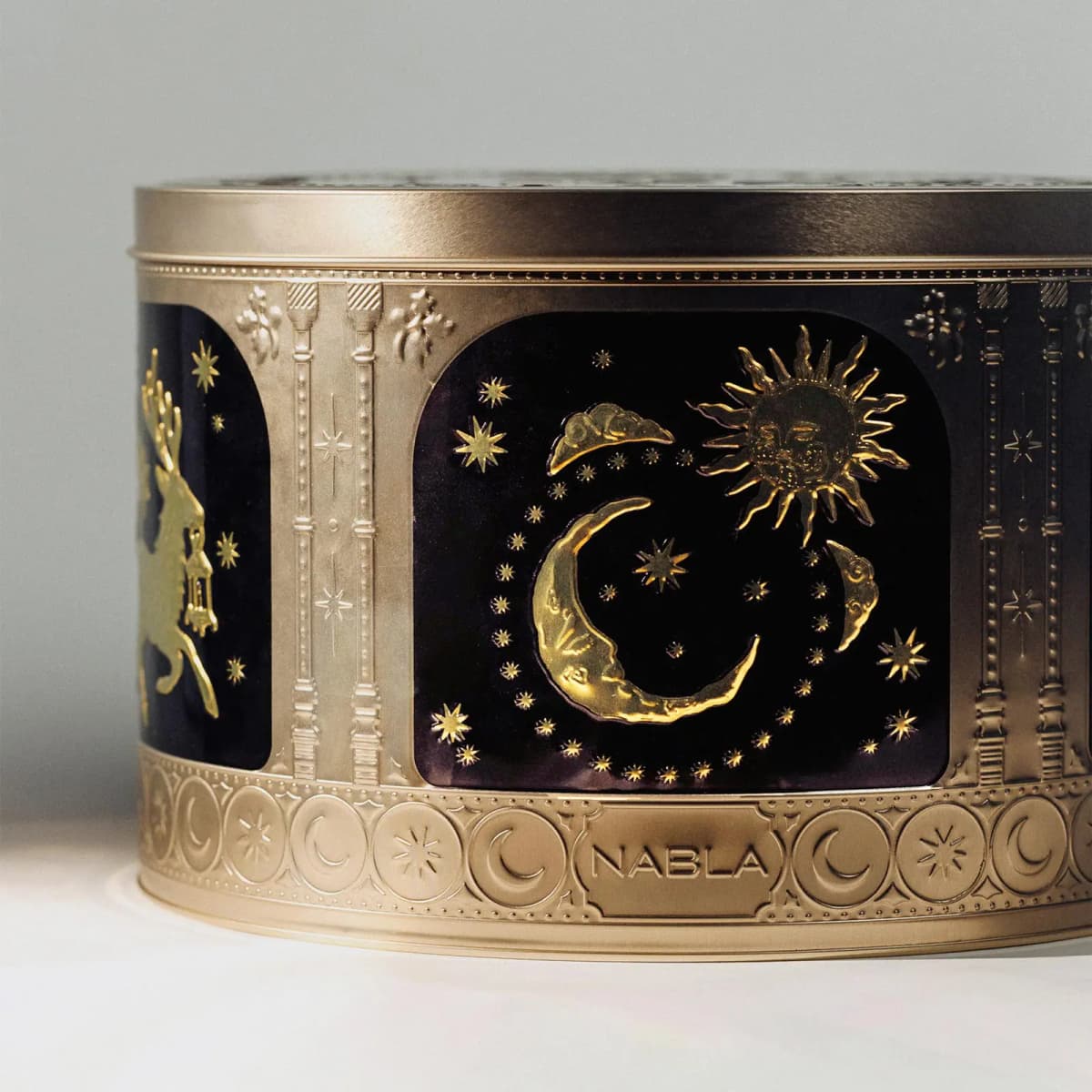 Close-up of the tin's embossed gold sun and crescent moon on black, beside a leaping deer panel