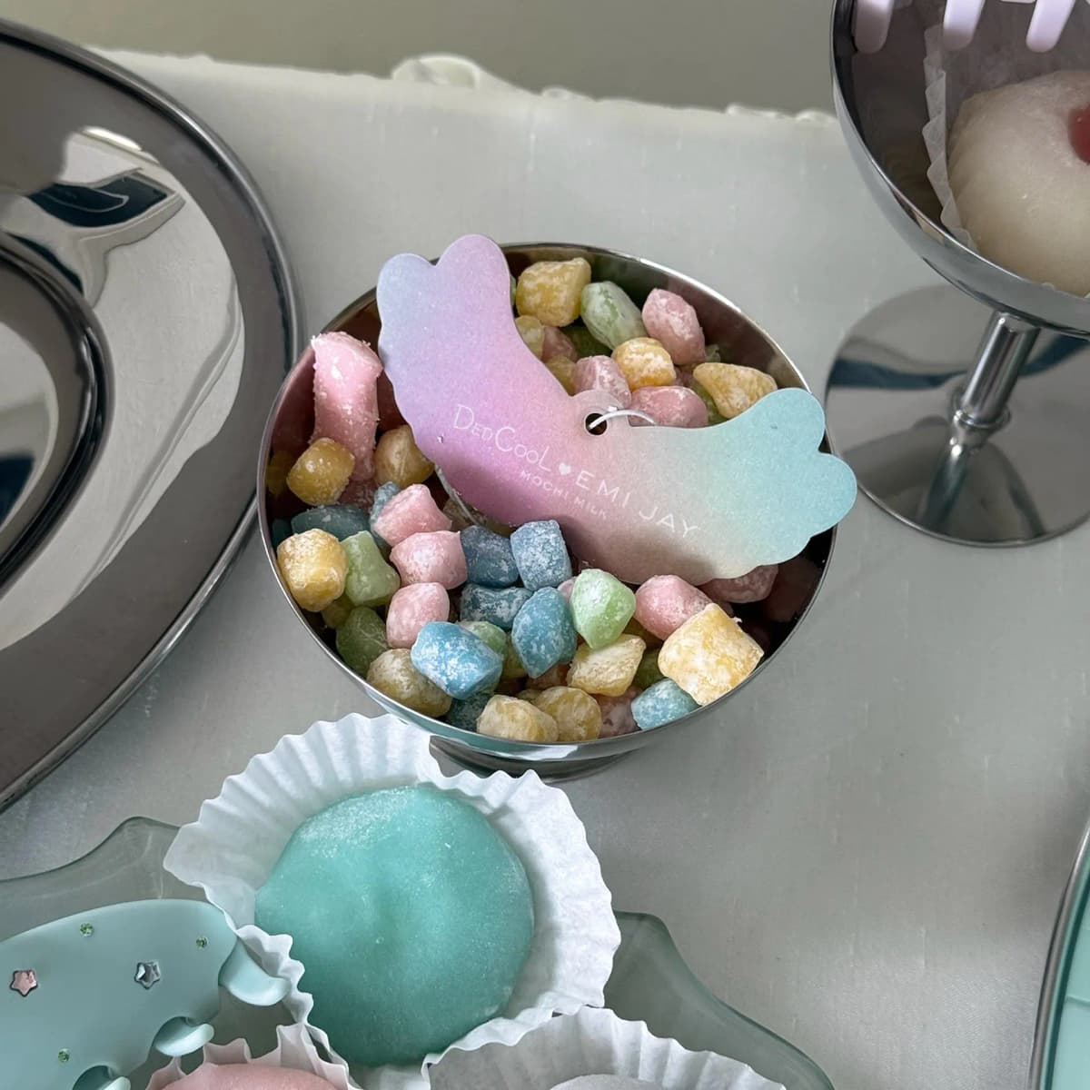 Pastel gradient angel-wing air freshener printed DedCool x Emi Jay Mochi Milk resting in a bowl of sugared candies