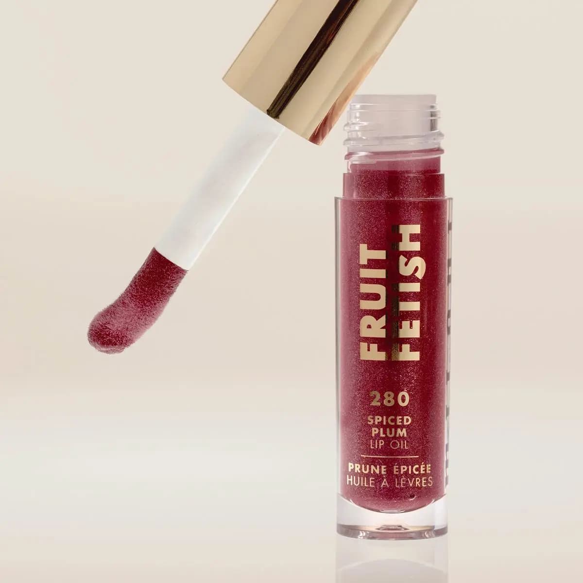 Spiced Plum applicator tilted above its open berry tube against a soft beige backdrop