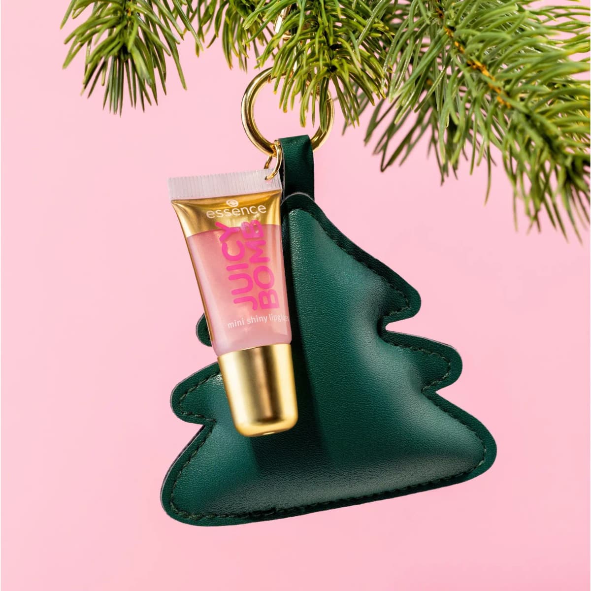 Mini lipgloss clipped to a green faux-leather tree charm hanging from a pine branch against a pink background