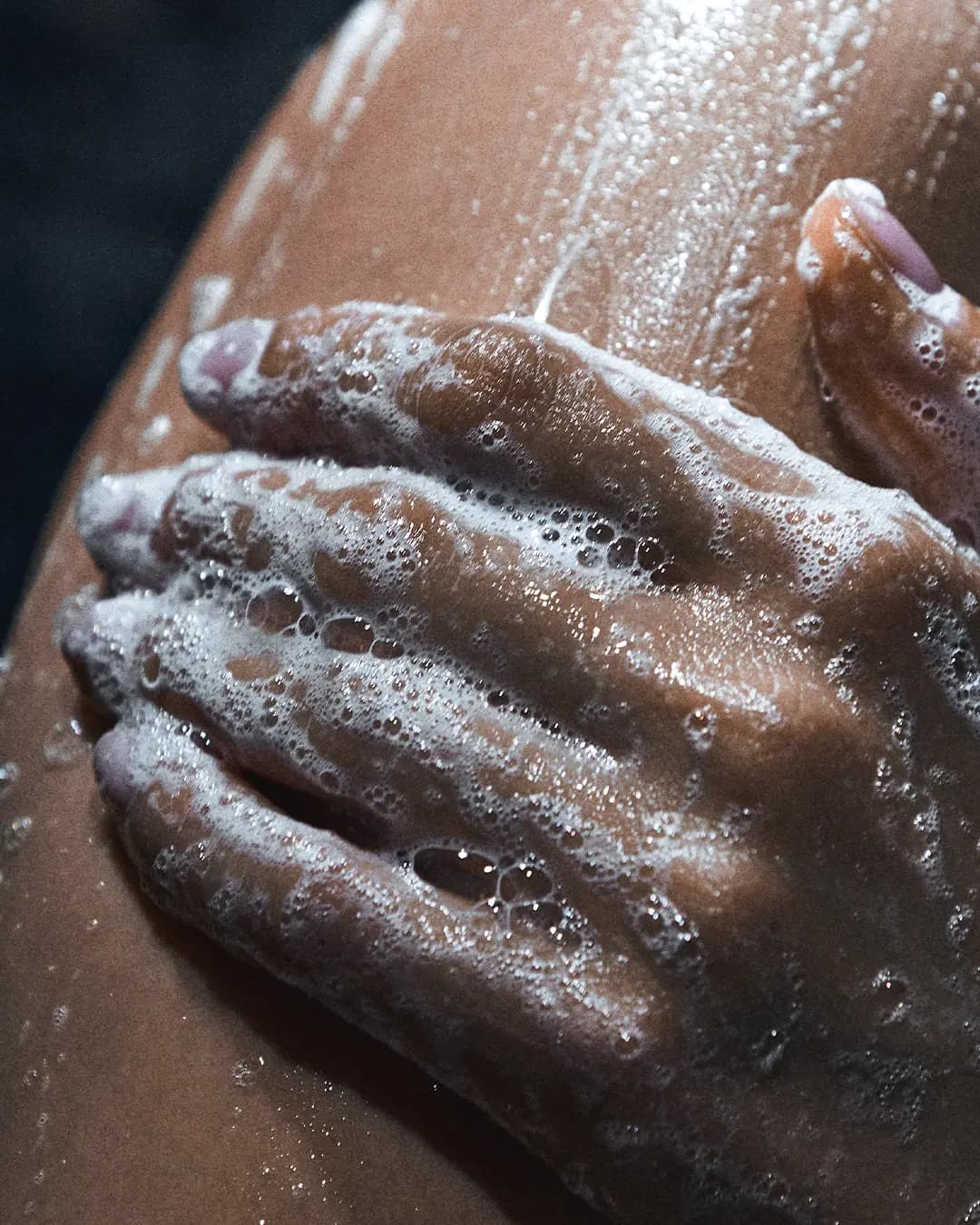 Close-up of a soapy hand lathering white foam over wet, glistening skin