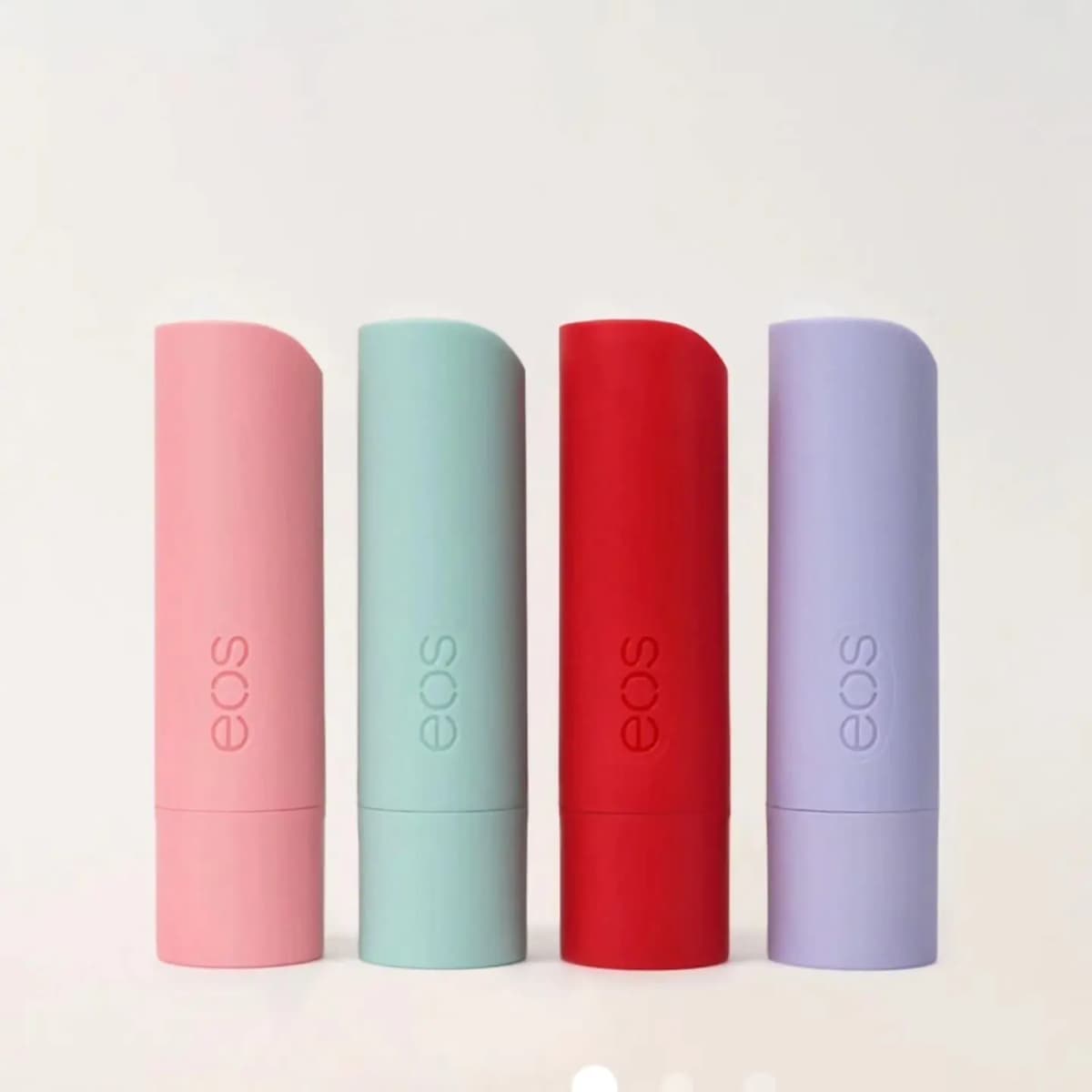 Four eos lip balm sticks in pink, mint, red and lavender standing in a row on a white background