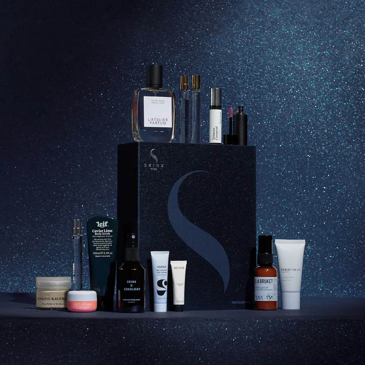Skins The Holiday Box gift box in glittery navy with perfumes, skincare and make-up minis on a sparkling blue backdrop