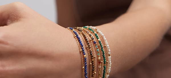 Stack of delicate gold chain and multicoloured beaded bracelets layered on a wrist