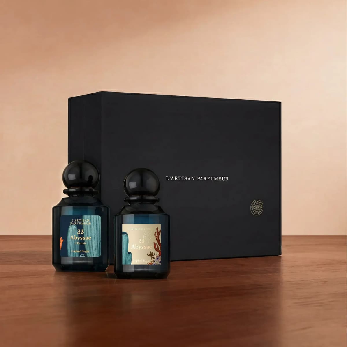 Abyssae L'Extrait and Abyssae Eau de Parfum bottles on a wooden surface before a black L'Artisan Parfumeur gift box