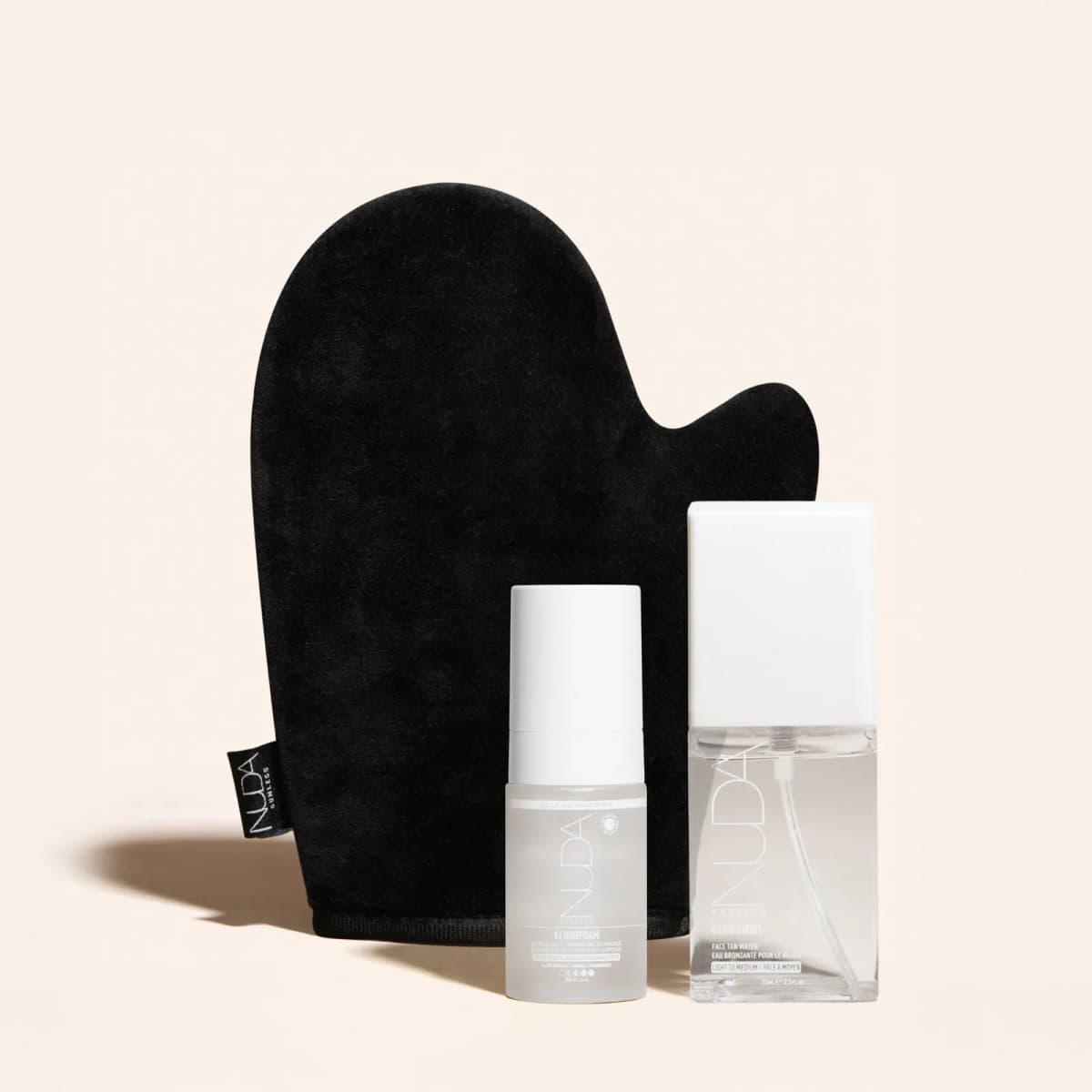 Black velvet NUDA tanning mitt behind a CloudFoam express mousse bottle and a CloudMist face tan water bottle.