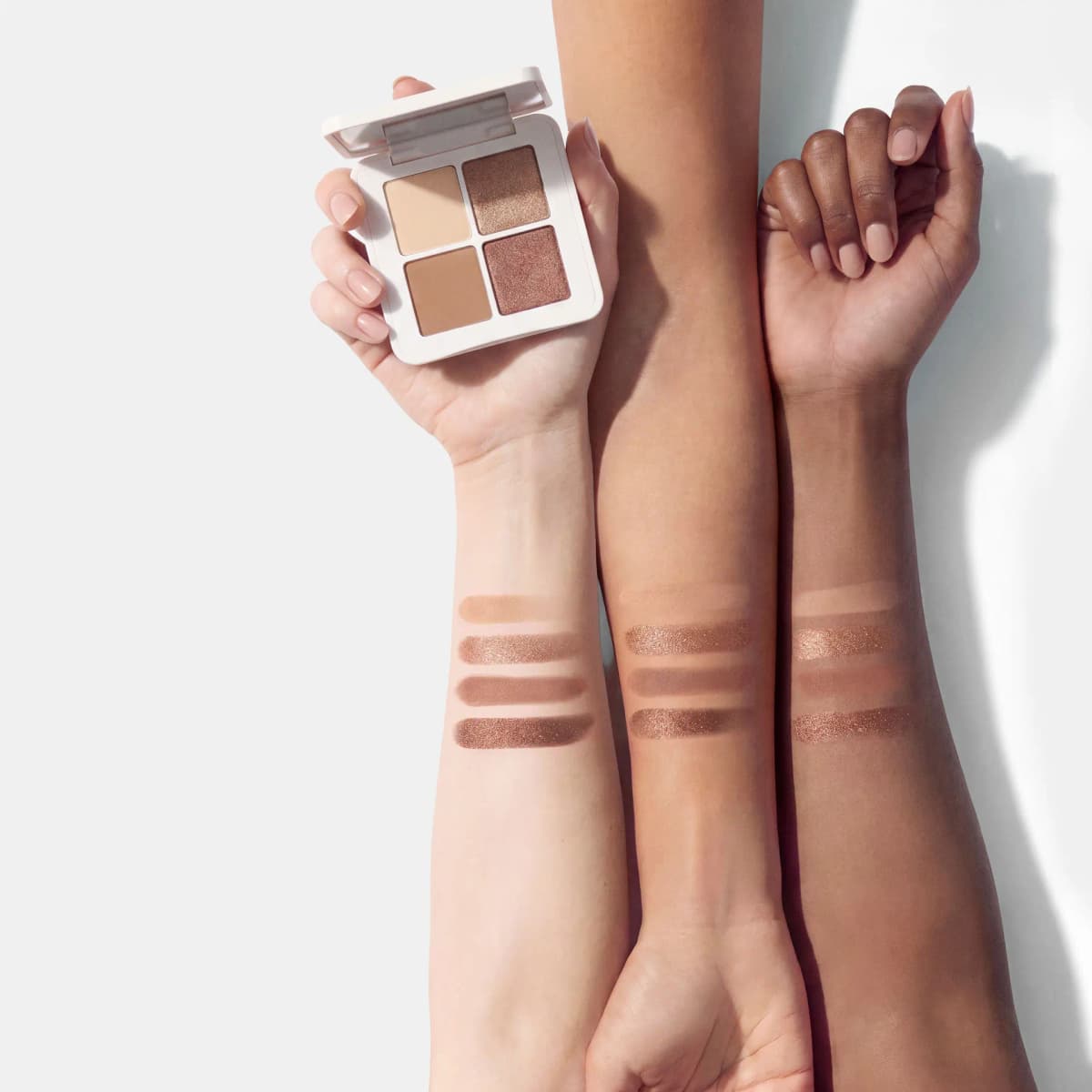 Warm eyeshadow quad held open above swatches of its four shades on light, medium and deep forearms