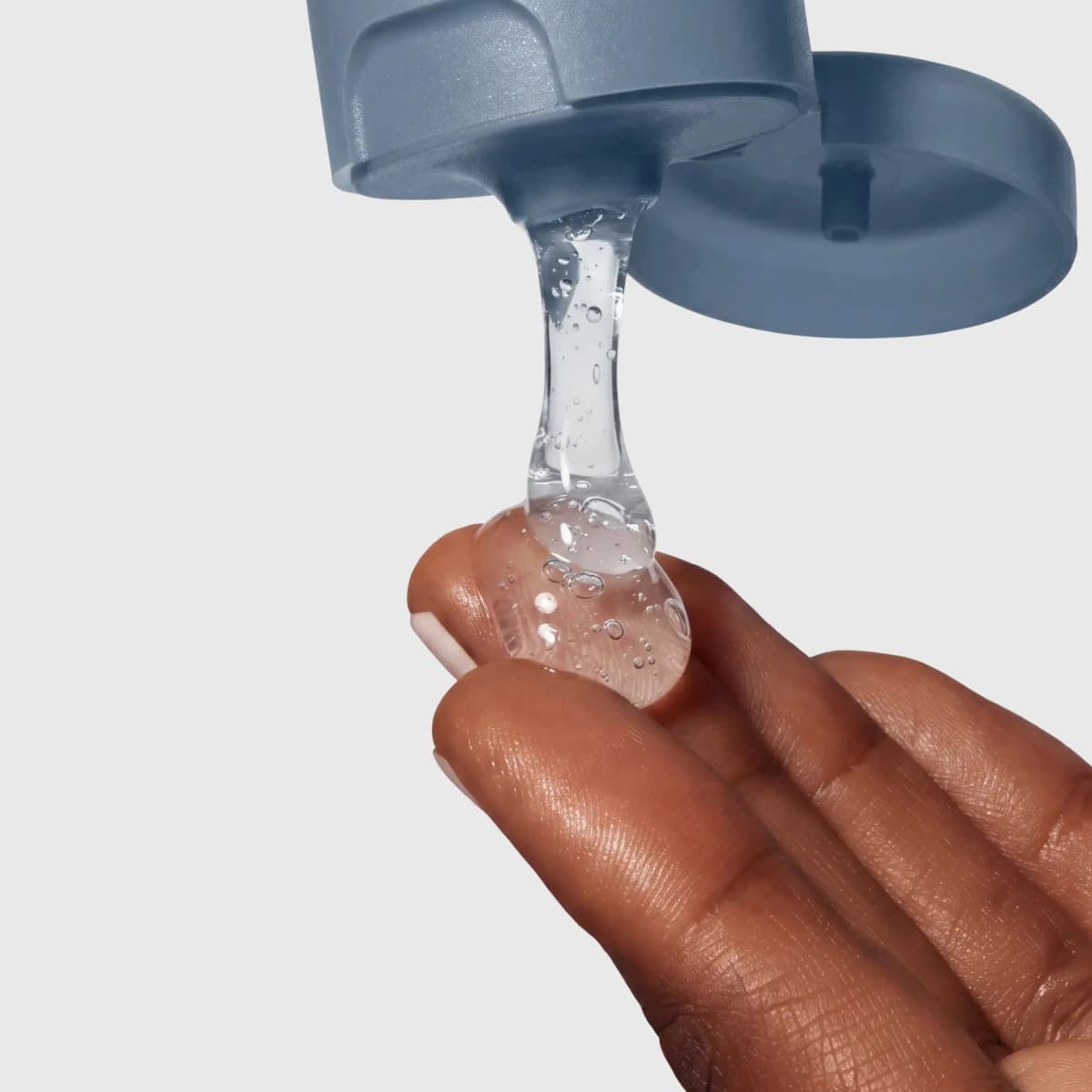 Clear bubbly cleanser gel pouring from the blue tube's flip cap onto fingertips