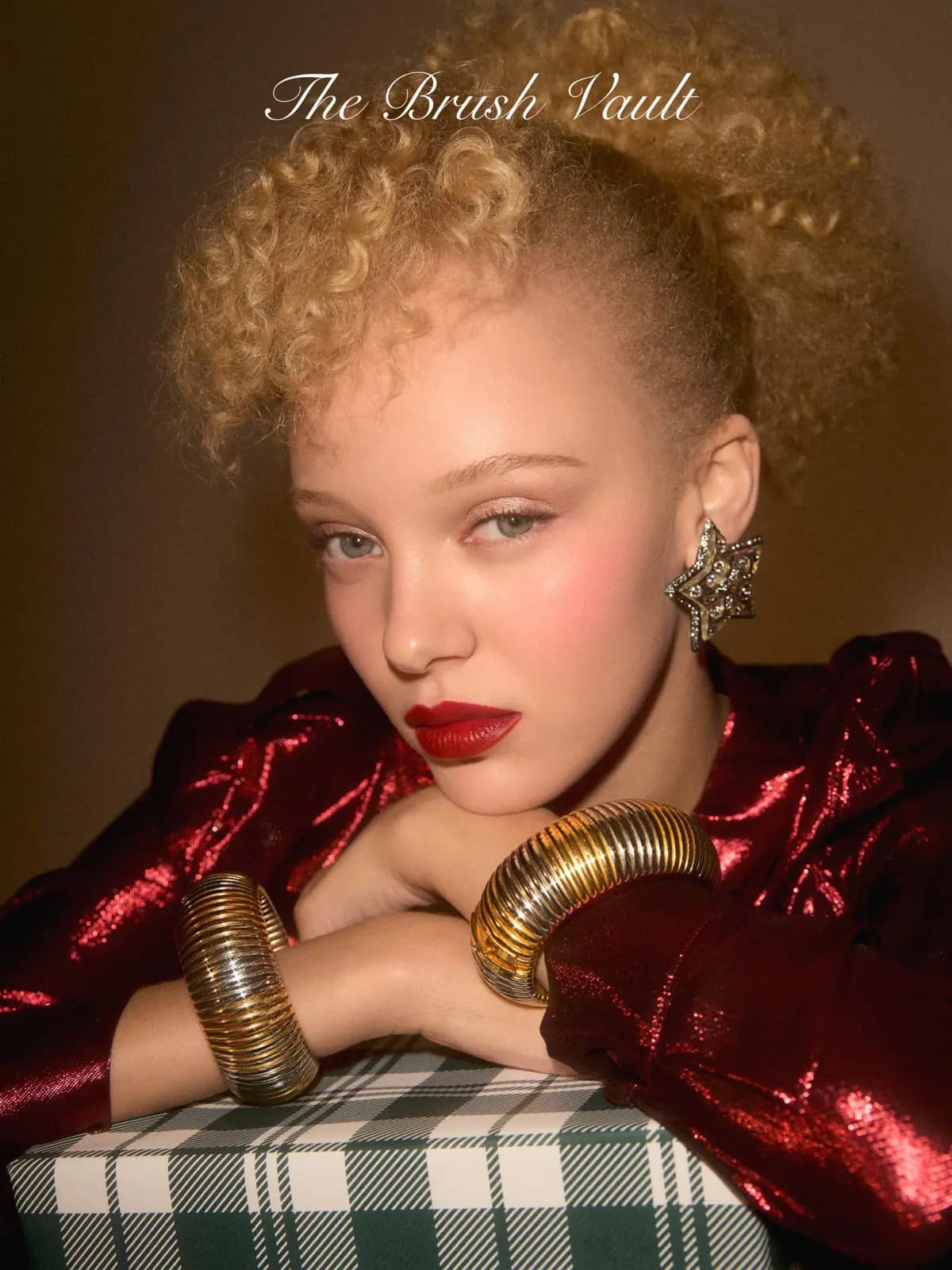 The Brush Vault campaign: blonde curly-haired model in red metallic jacket, red lips, gold cuffs, plaid gift box