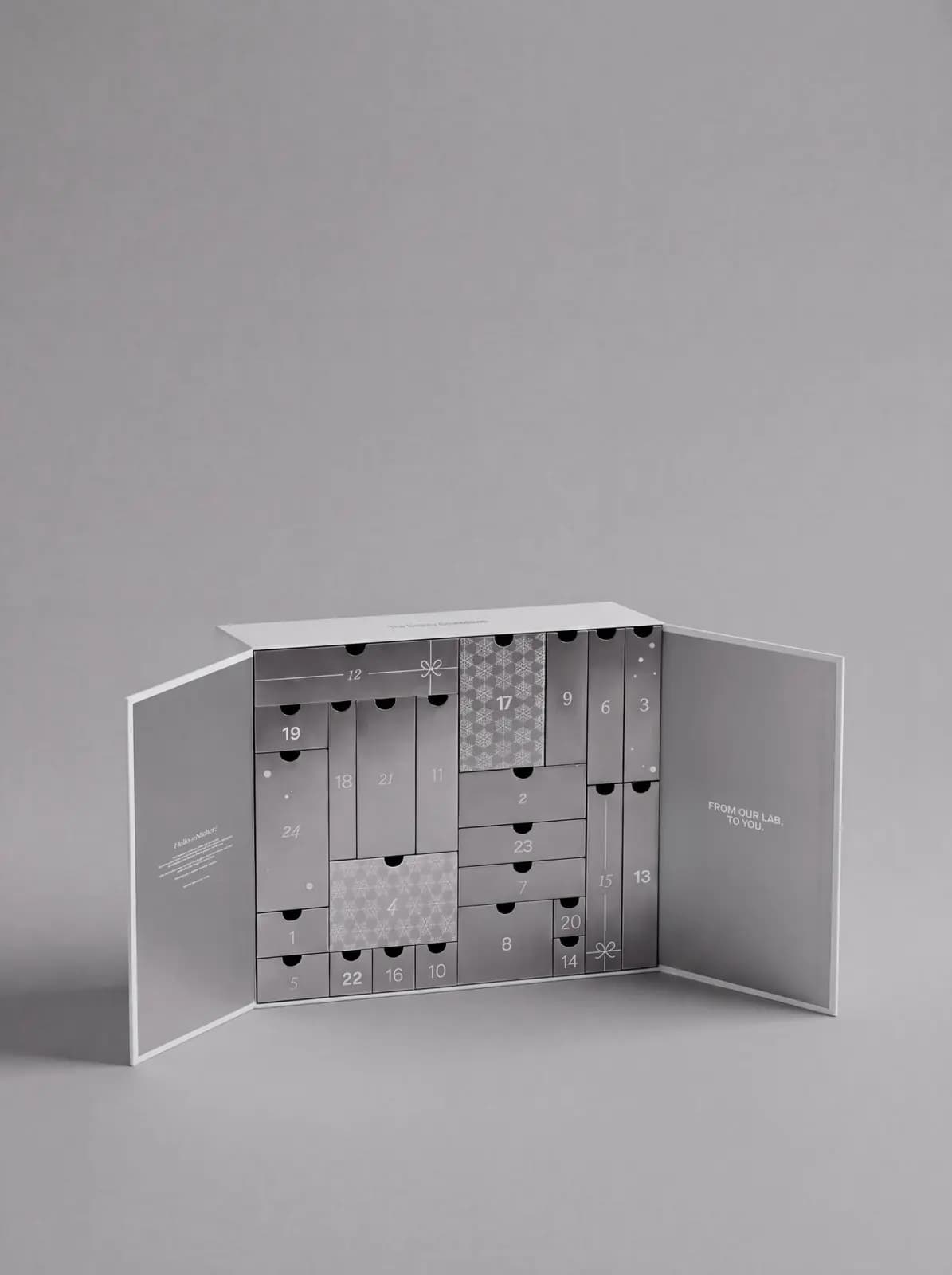 Open silver advent calendar revealing numbered grey drawers with snowflake and bow accents