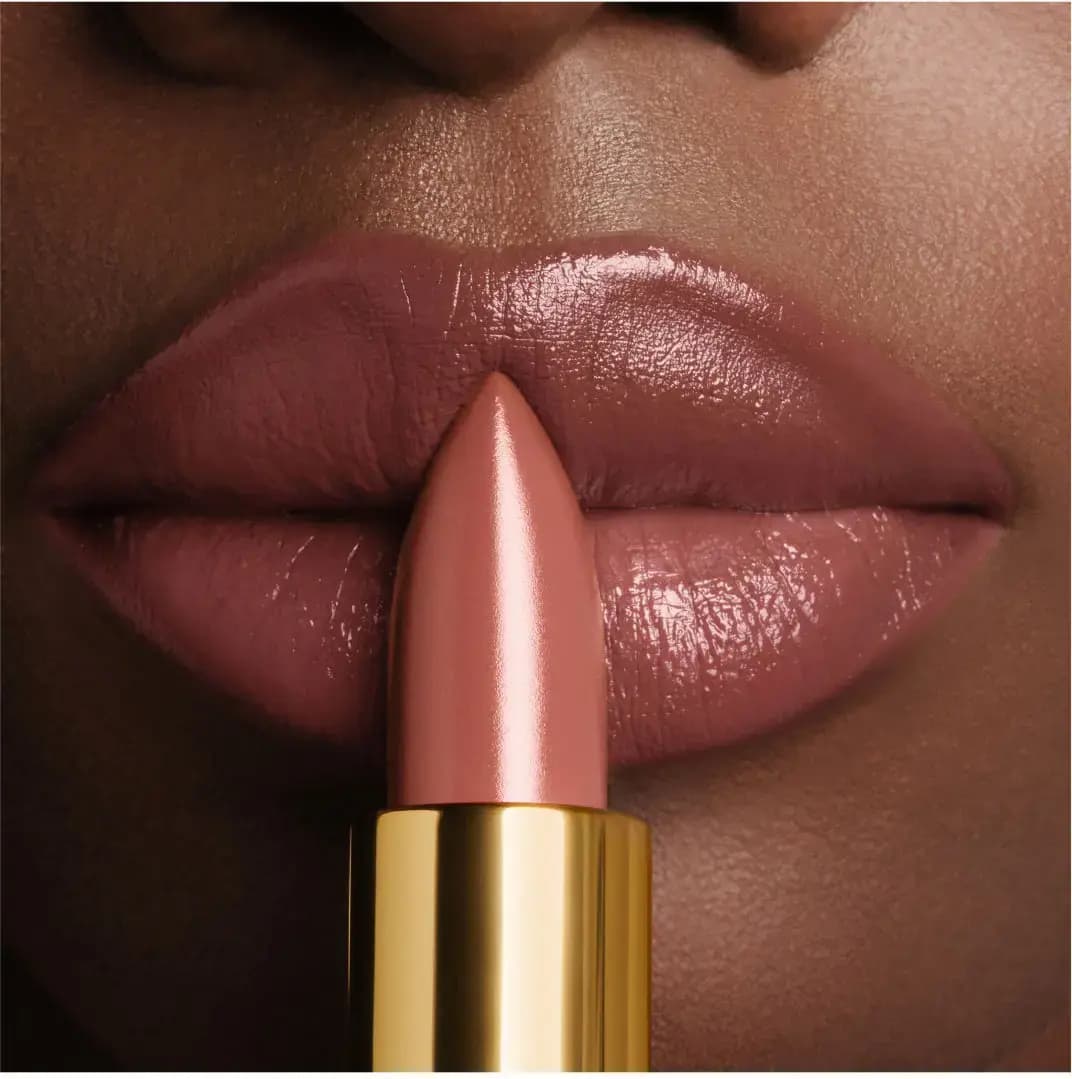Close-up of glossy rosy nude lips on deep skin with a matching lipstick bullet held in front