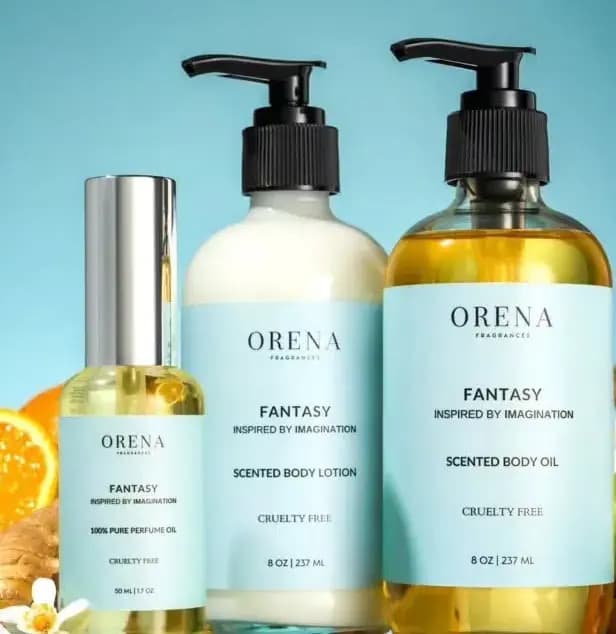 Fantasy perfume oil, body lotion and body oil with pale blue labels beside orange slices and ginger on a sky-blue backdrop