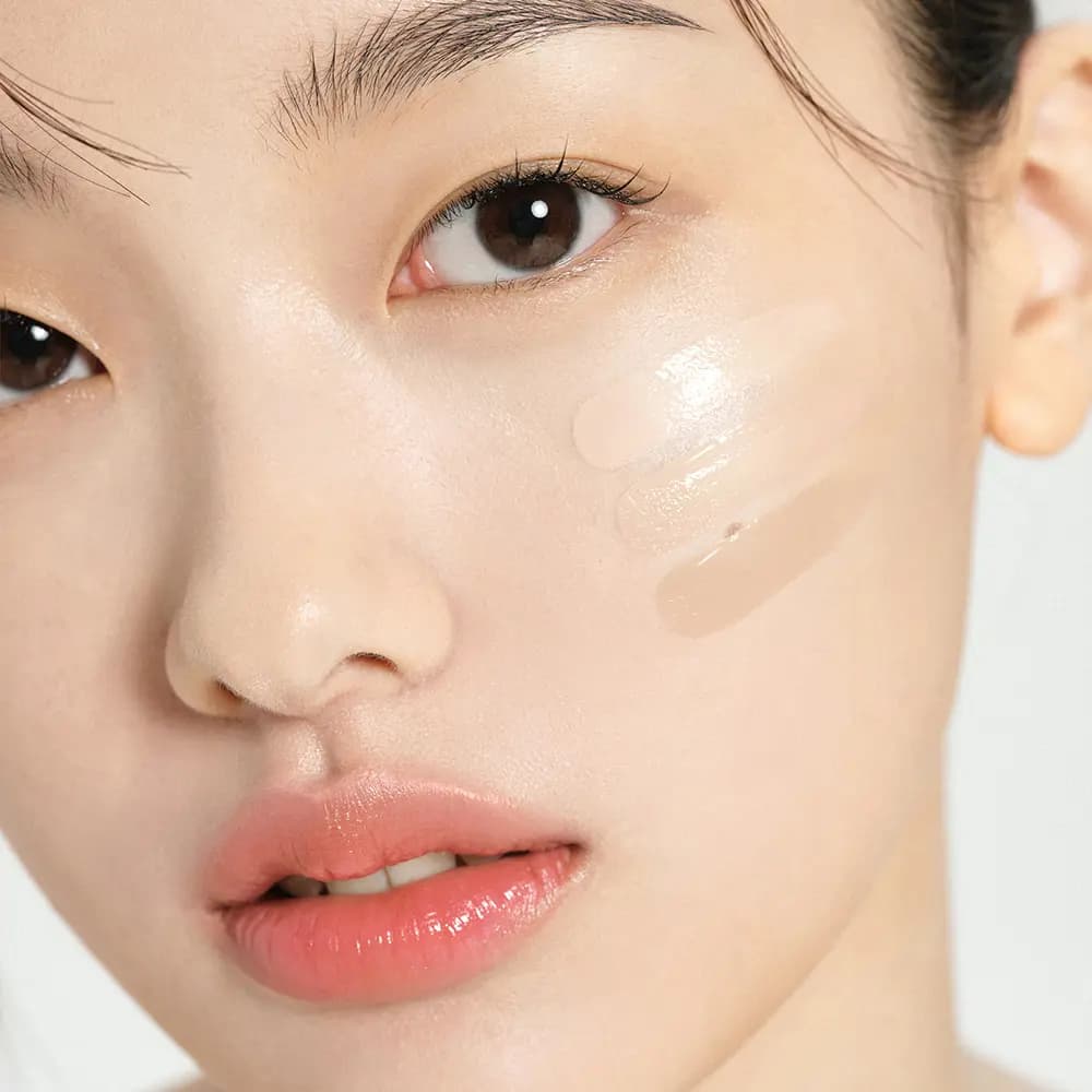 Close-up of a model's cheek with three strokes of glossy beige BB cream swiped beneath the eye