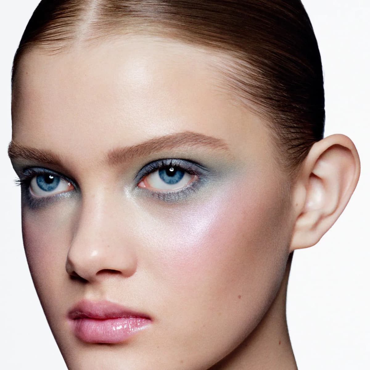 Model with slicked-back hair wearing smoky blue-grey shadow and lilac shimmer on the cheekbones