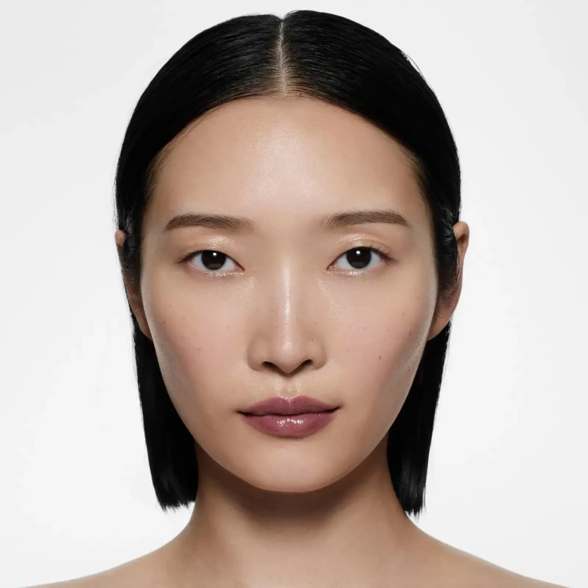 Model with a sleek black bob and dewy skin wearing a shiny mauve-plum lipstick