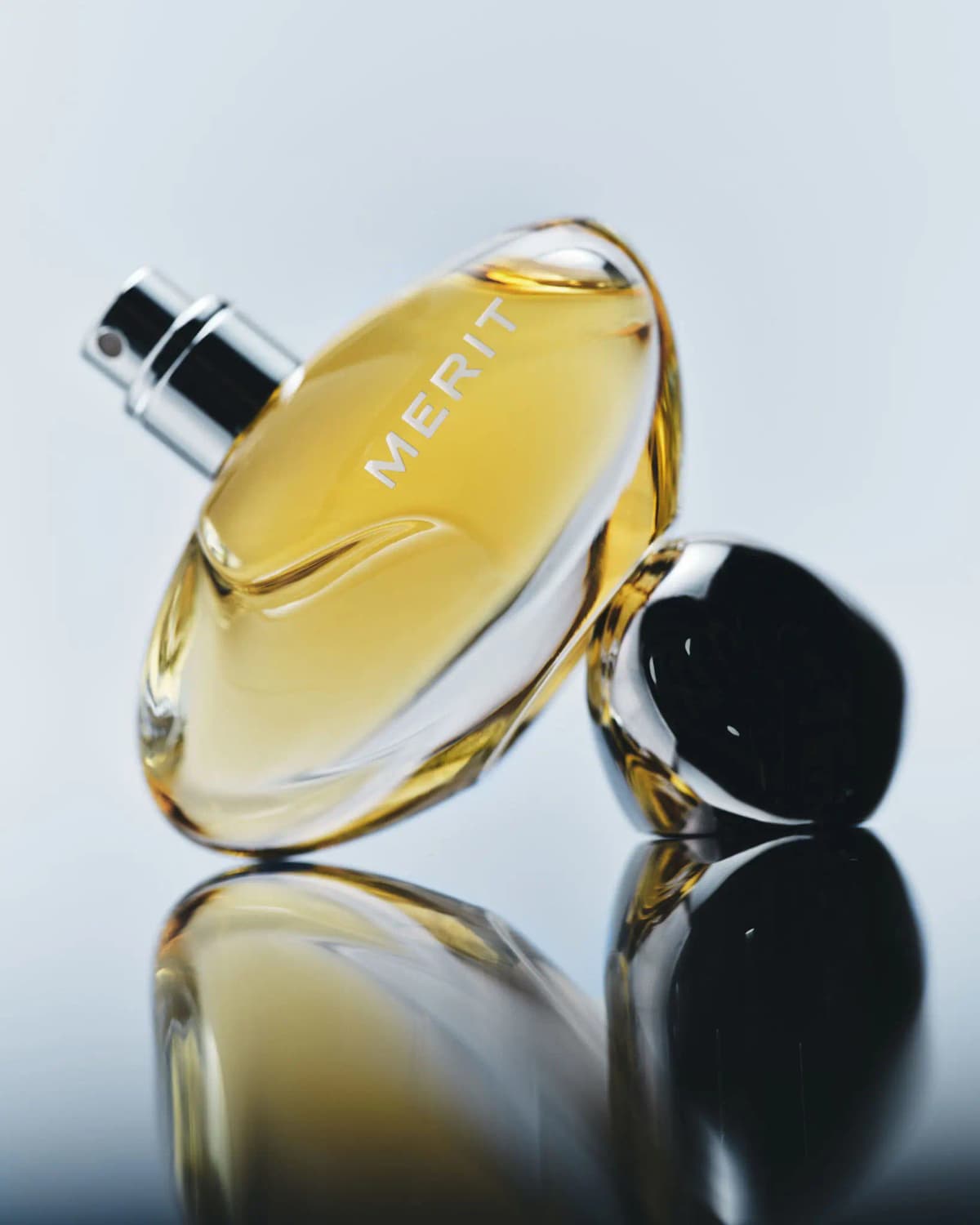 Uncapped bottle tilted to show its silver spray nozzle, leaning on the chrome cap over a reflective surface