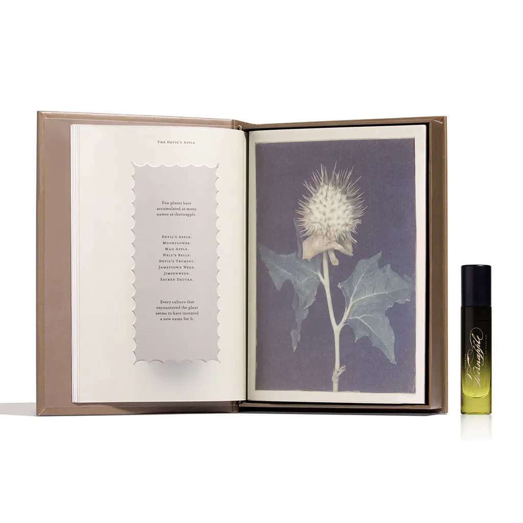 Open book showing 'The Devil's Apple' list of thornapple names and a spiky seed pod print, with the 5ml vial beside it.
