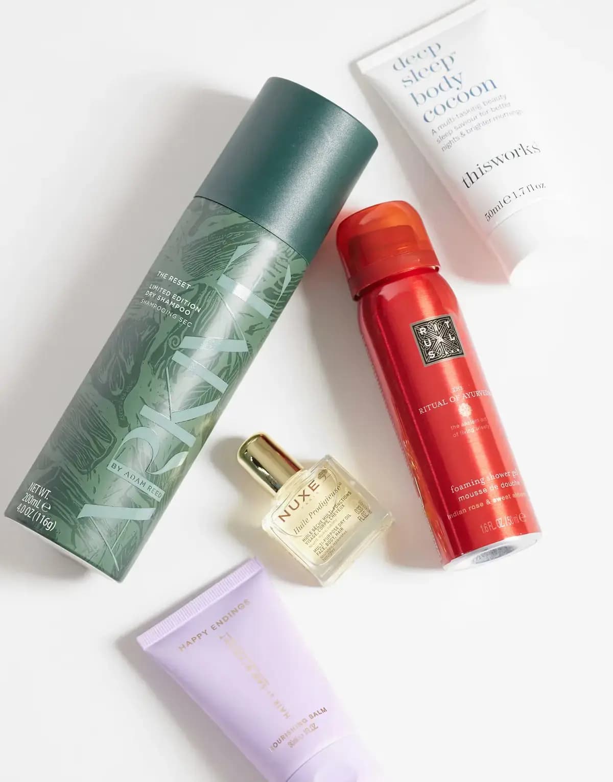 Flat lay of green Arkive dry shampoo can, NUXE oil bottle, red Rituals shower foam, This Works and lilac Happy Endings tubes
