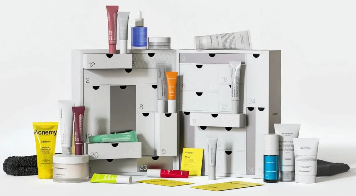 Full display of an open advent calendar with numbered drawers surrounded by skincare tubes, serums, cleansers and accessories