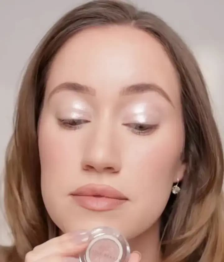 Ravie Beauty founder Allie Glines with pale pink glistening shimmer on both lids, holding an open Softlight eye topper compact