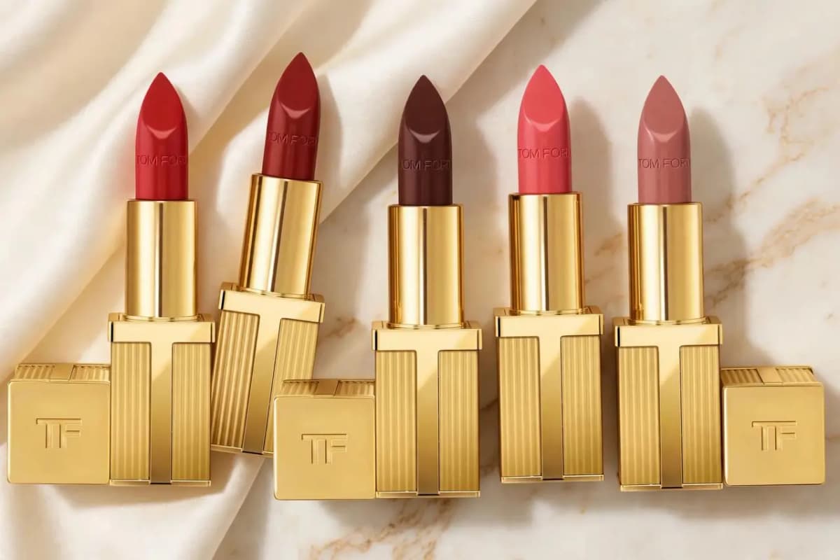 Five Tom Ford lipsticks in gold cases, red, deep red, dark brown, coral and rosy nude, on cream satin and marble