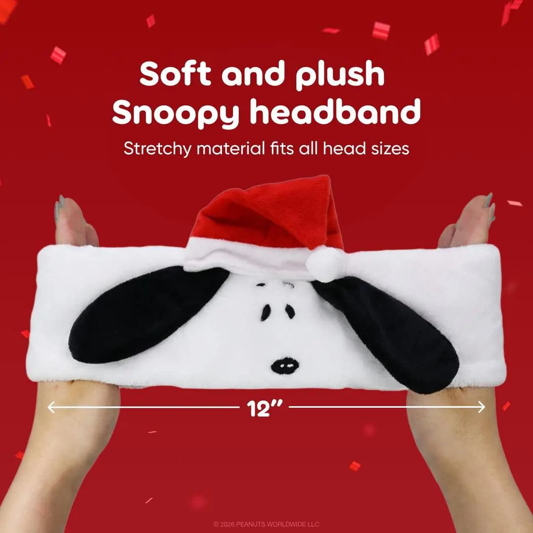 Hands stretching the plush Snoopy Santa headband on red, labelled 12 inches and fits all head sizes.