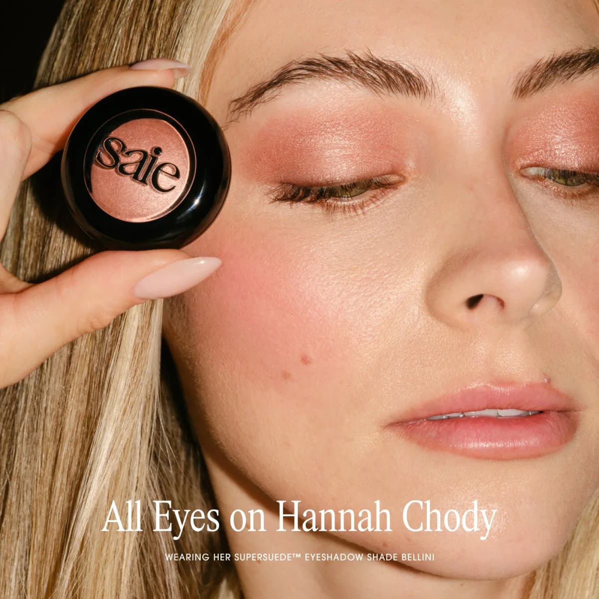 Hannah Chody holds a Saie compact near the face, wearing rosy shimmer eyeshadow in Bellini with matching blush