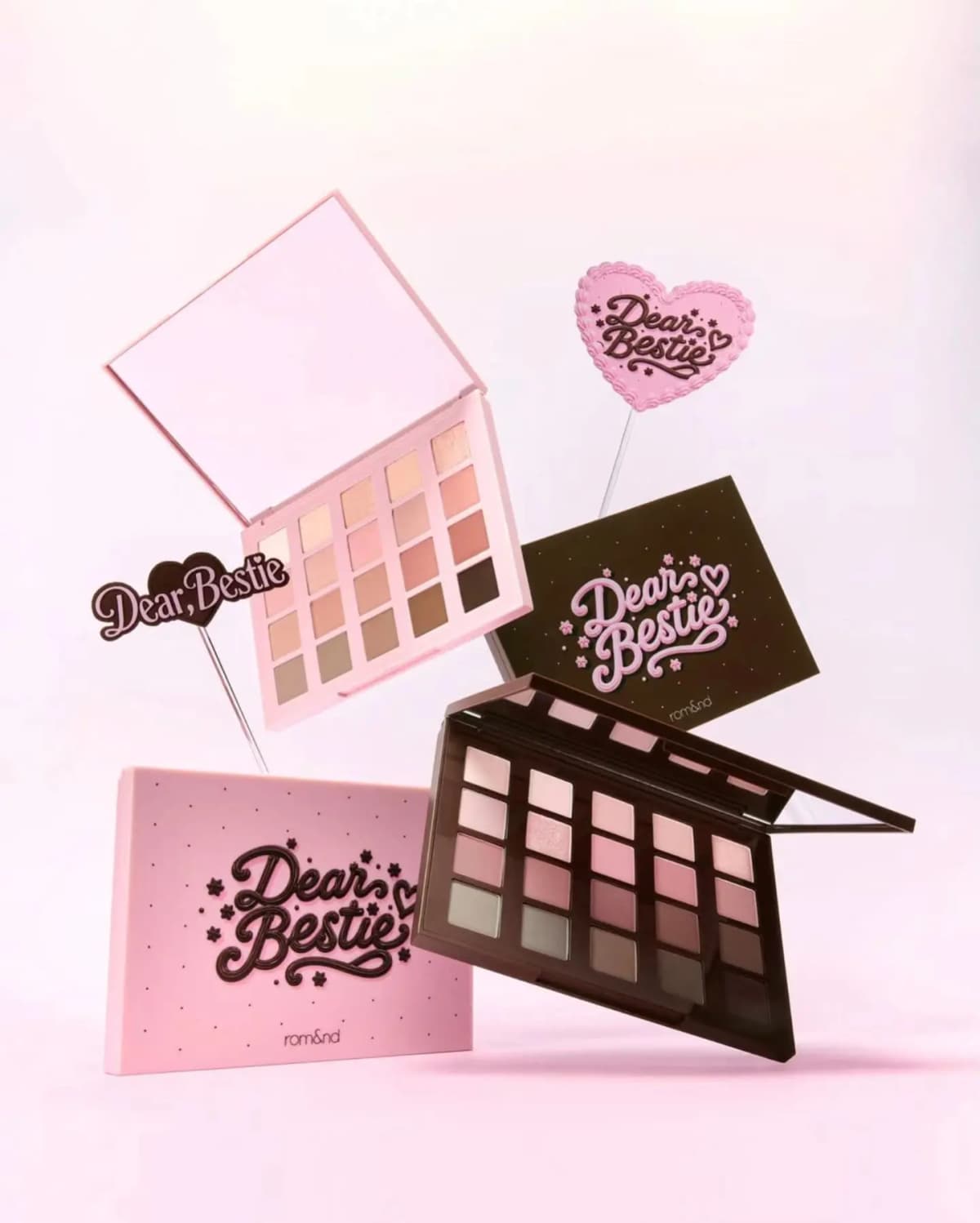 Two Dear Bestie 20-shade palettes, one pink with peachy neutrals and one brown with rosy mauves, floating with heart toppers