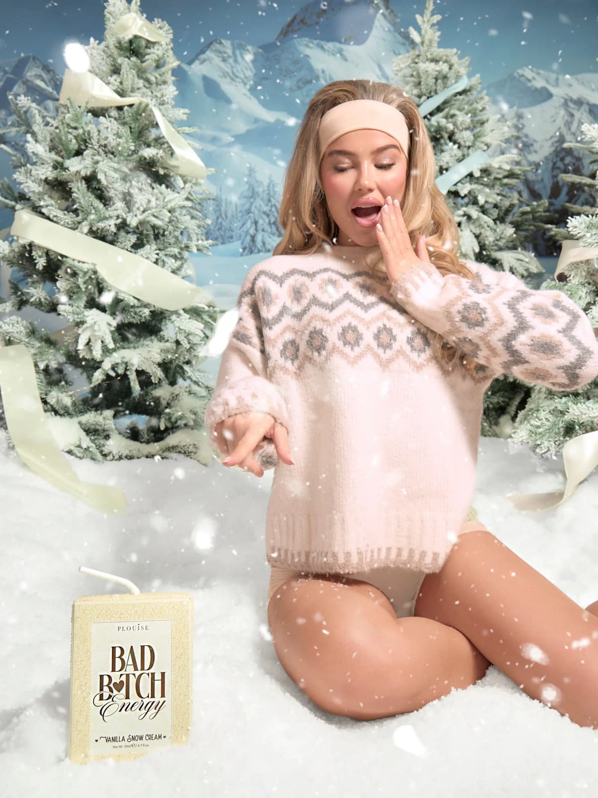 Model in cream fair-isle sweater kneeling in snow beside a Vanilla Snow Cream Bad Bitch Energy pack.