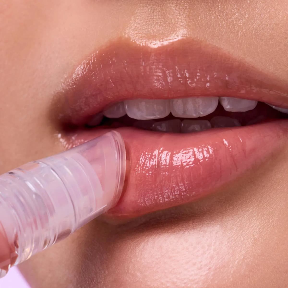 Clear applicator touching a sheer, glossy peachy-pink lower lip on light skin