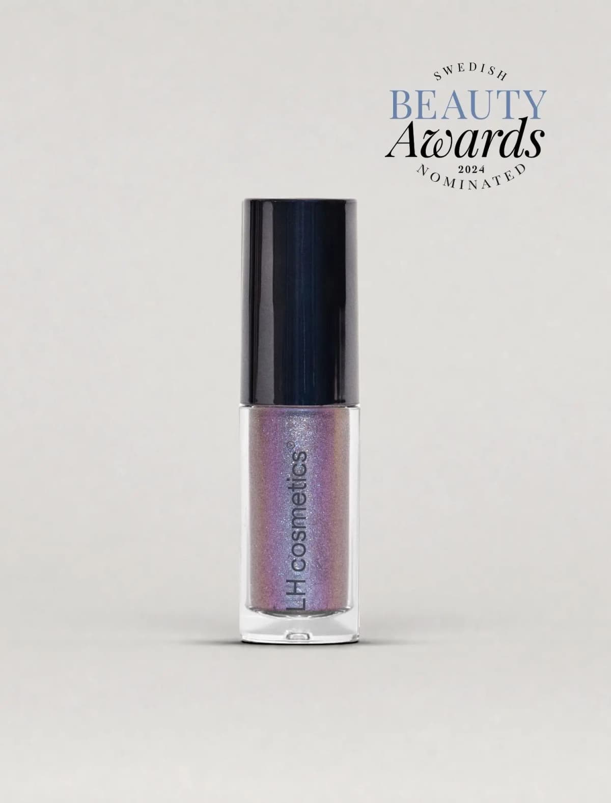 Tube of violet liquid shadow with blue and pink shimmer, black cap and Swedish Beauty Awards nominee badge