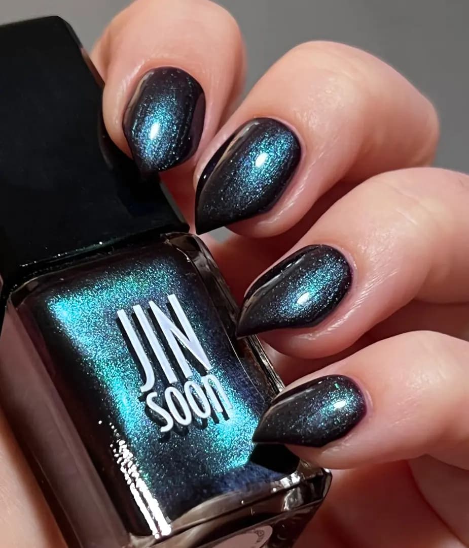 Close-up of nails in dark polish with blue-green shimmer beside a JINsoon bottle glowing teal
