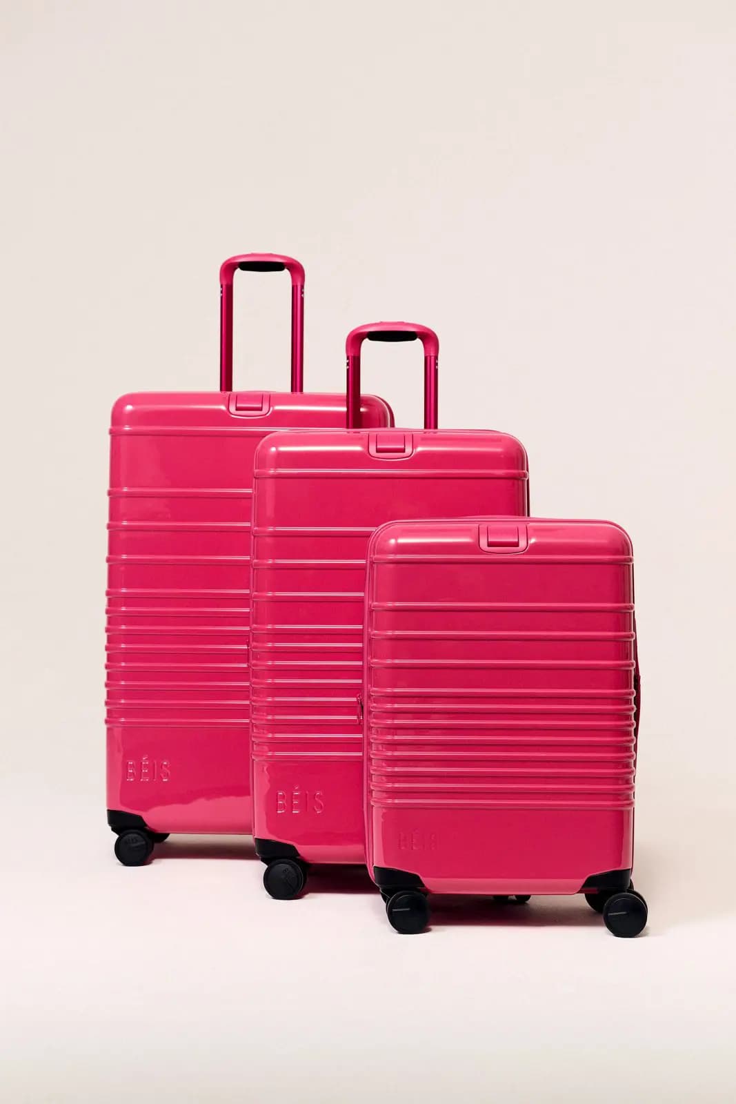 Three glossy raspberry BÉIS hard-shell suitcases in large, medium and carry-on sizes