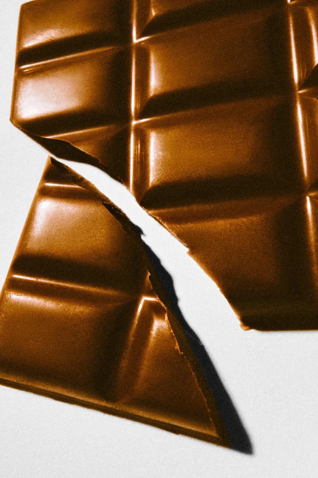 Glossy milk chocolate bar snapped in two diagonally on a white background