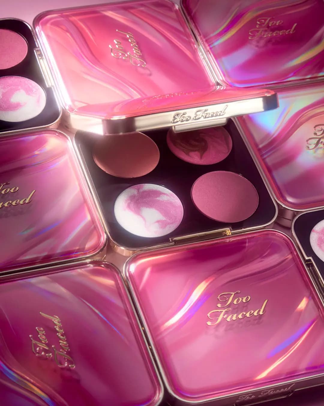 Multiple marbled pink compacts arranged together, one open to show four blush and highlighter shades.