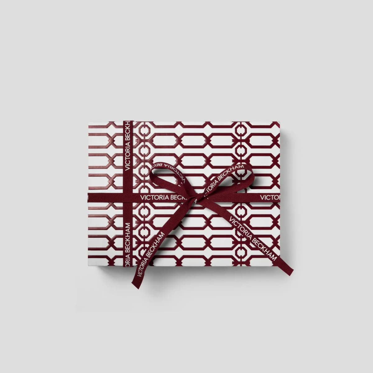 Top view of white gift box with burgundy geometric chain print, tied with a Victoria Beckham ribbon bow