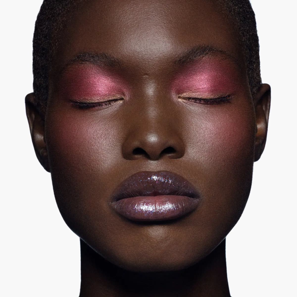 Model with eyes closed wearing shimmering raspberry-pink shadow, flushed cheeks and sparkly plum gloss