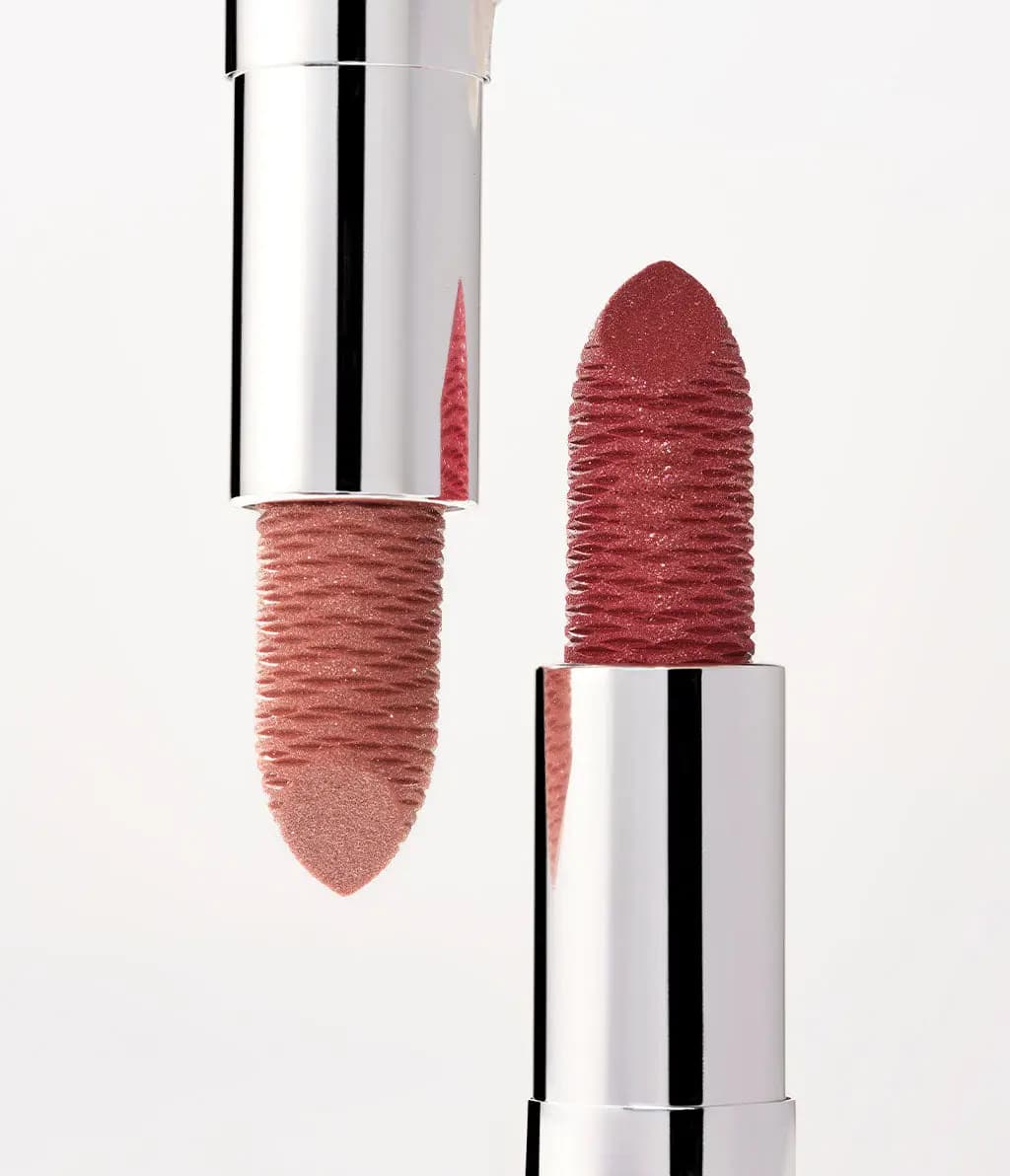 Close-up of two textured glitter lipsticks, nude pink and berry red, in mirrored silver cases