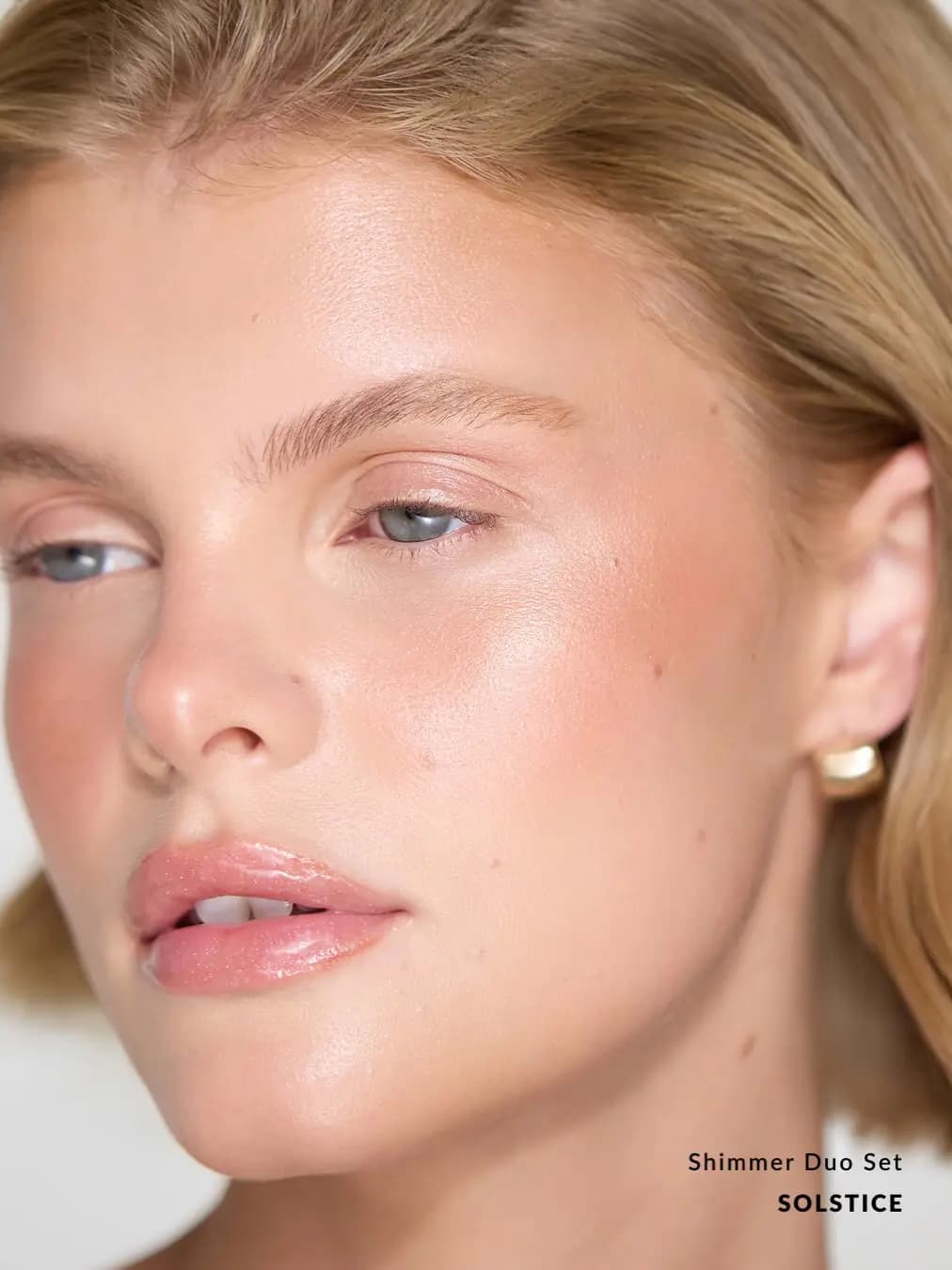 Close-up of a blonde model with glowing cheeks and glossy lips wearing the Solstice Shimmer Duo Set.