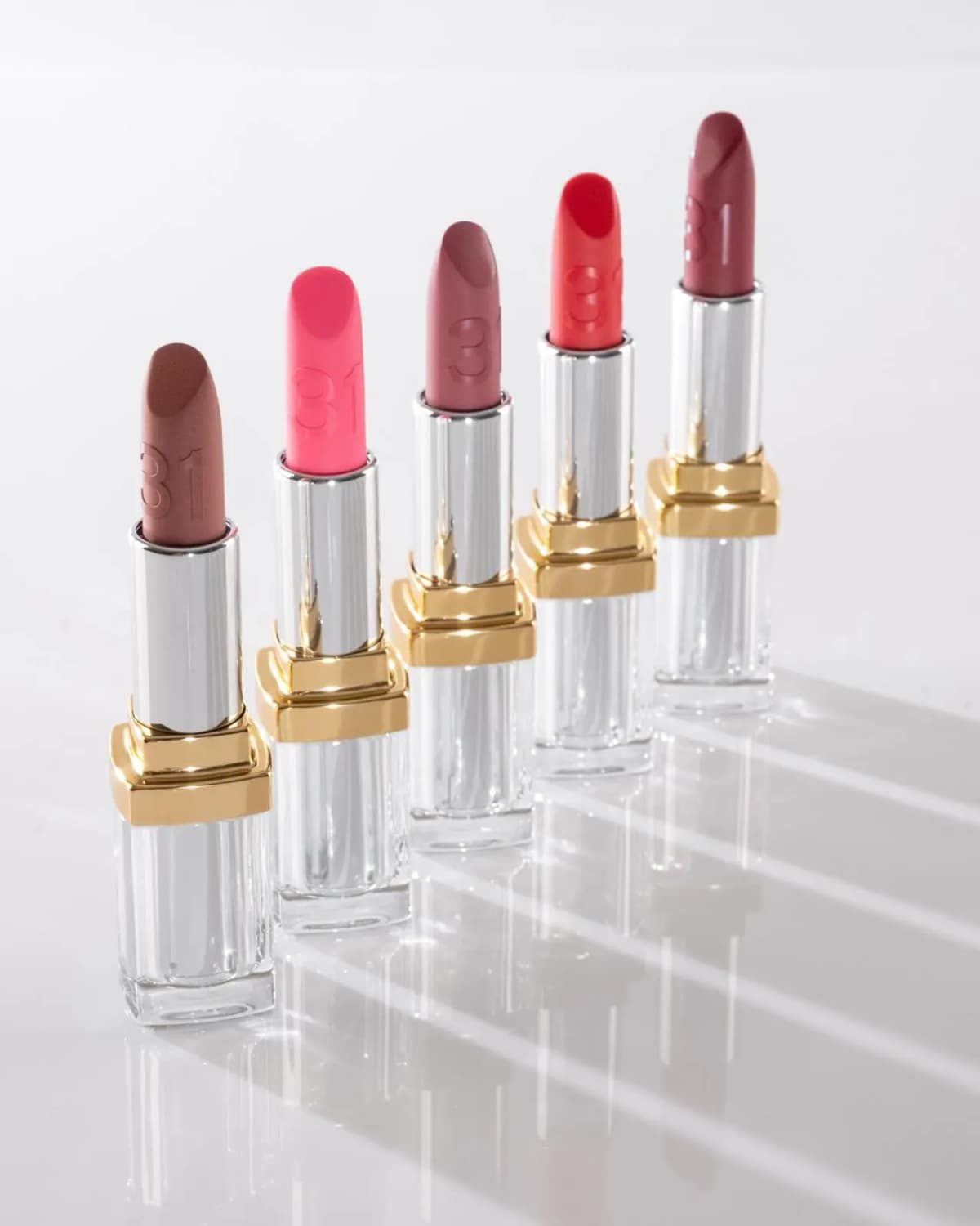 Chanel 31 Le Rouge Supreme Lip Nos. 25 to 29 lined up diagonally in faceted clear and gold cases