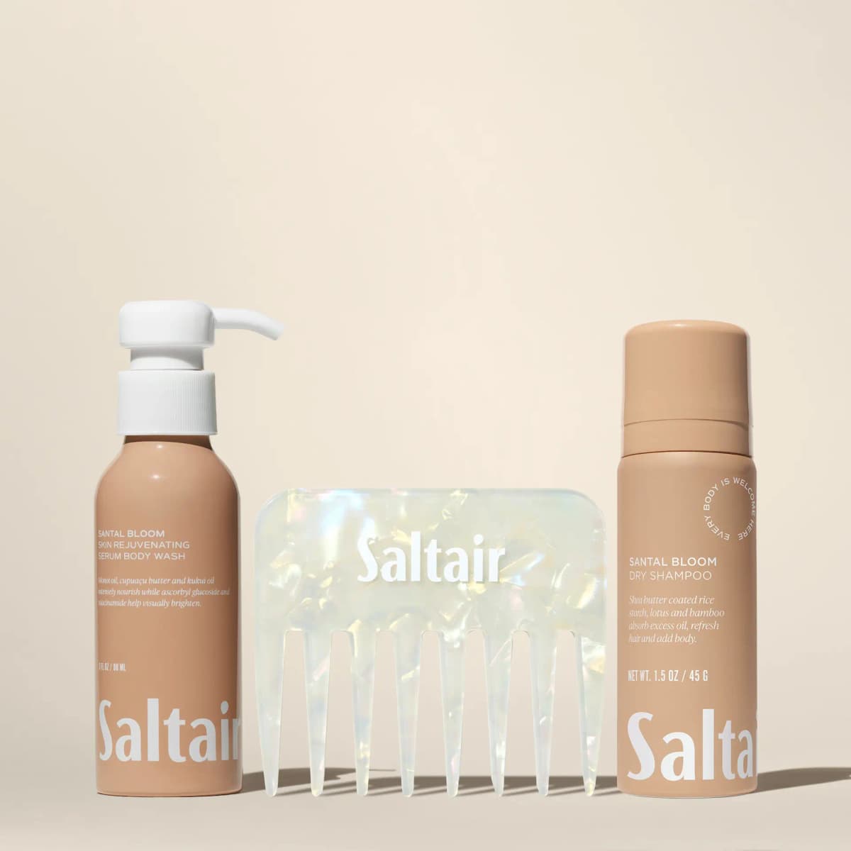 Tan pump body wash, iridescent Saltair wide-tooth comb and tan dry shampoo can lined up on a cream backdrop