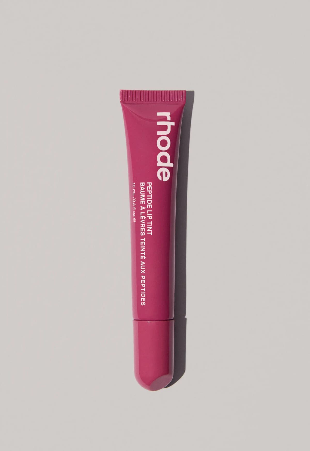 Berry-magenta rhode Peptide Lip Tint tube with pale pink text casting a soft shadow on grey