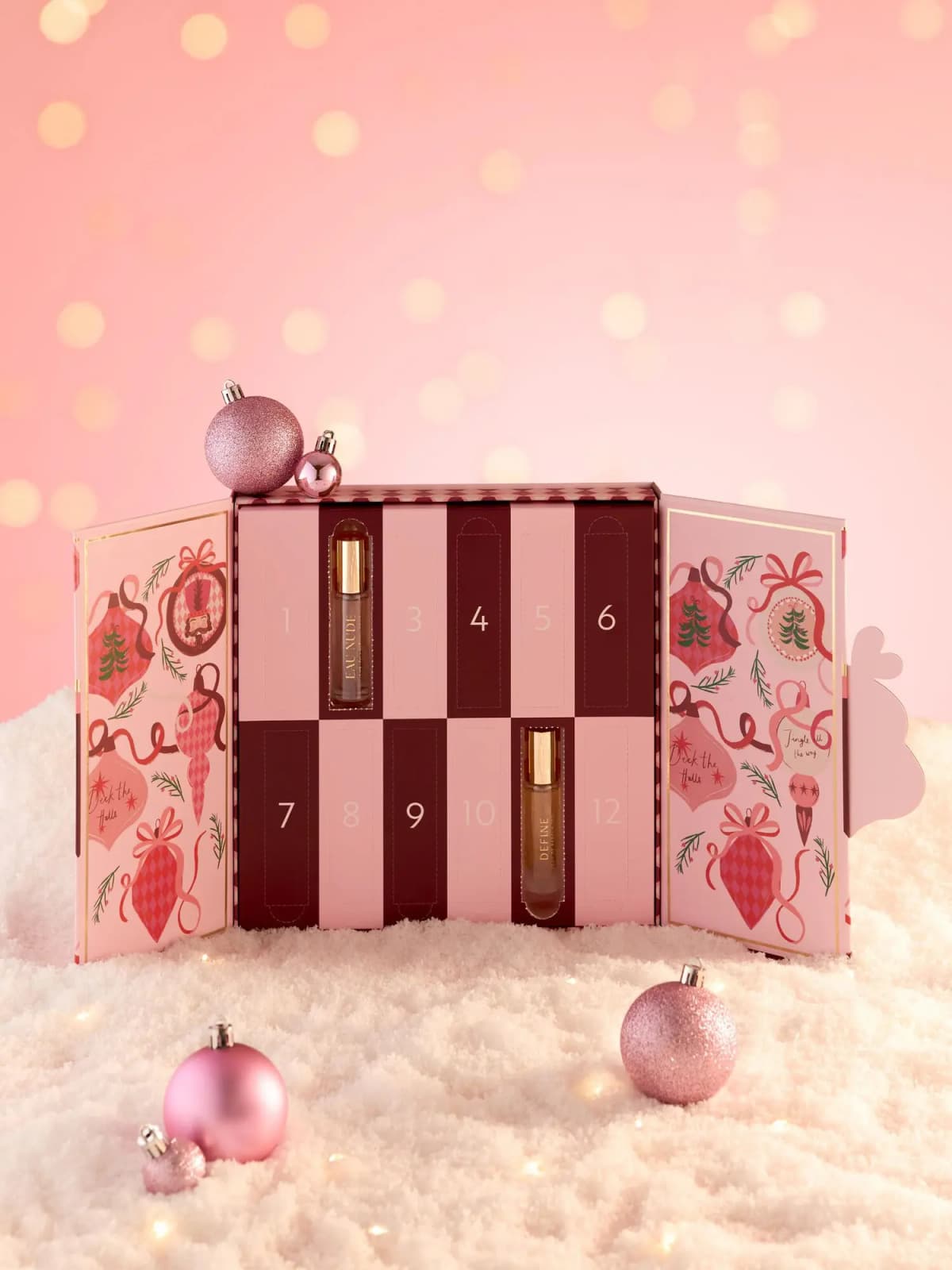 Advent calendar opened to pink and burgundy numbered doors, Eau Nude and Define bottles revealed, pink baubles in snow