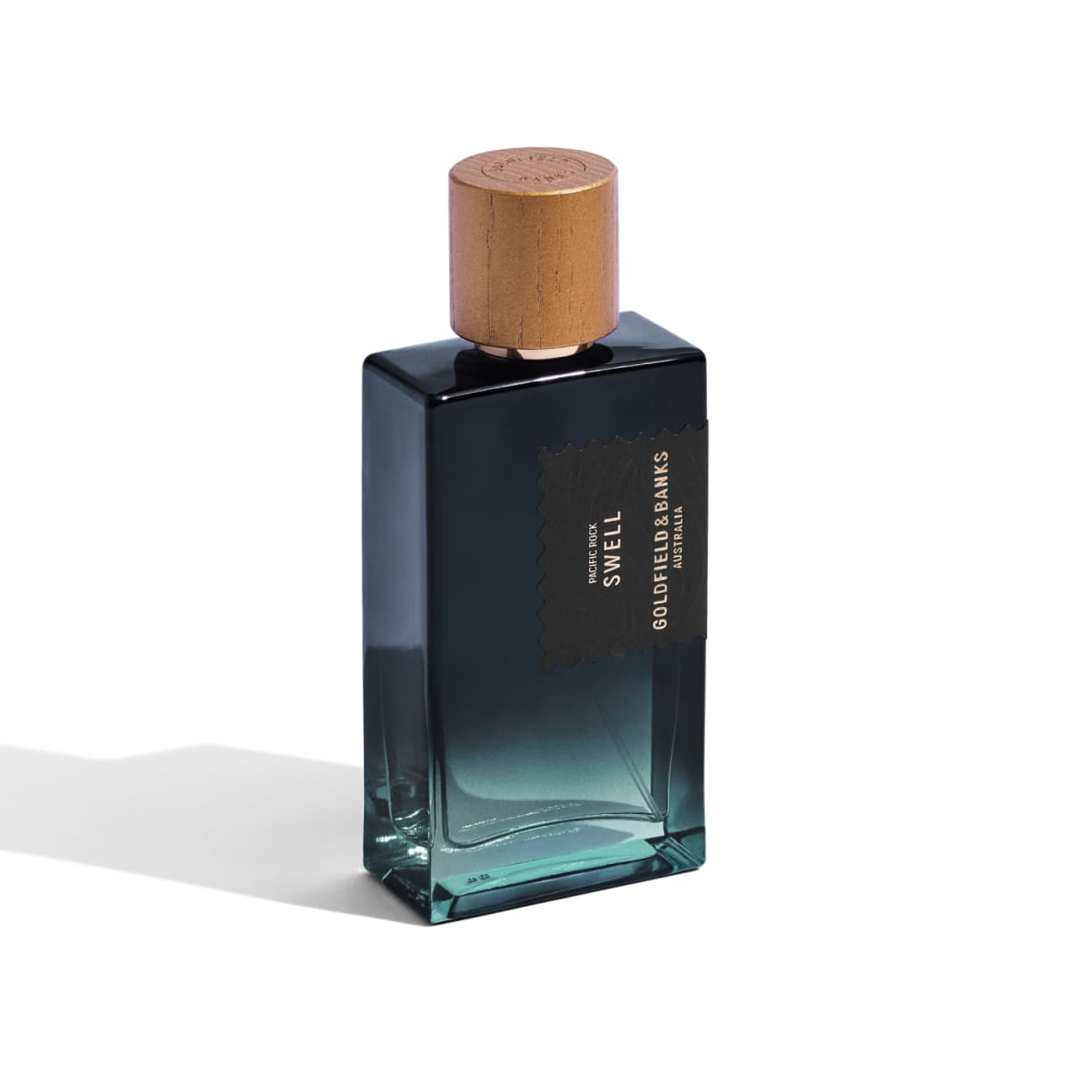 Tall 100ml Pacific Rock Swell bottle in navy-to-teal gradient glass with wooden cap on a white background