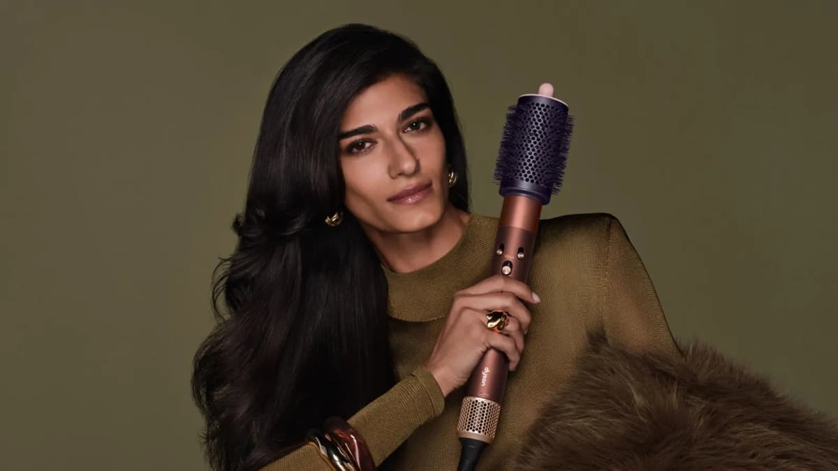 Model with long dark blowout in an olive knit holding a copper multi-styler fitted with a plum round brush